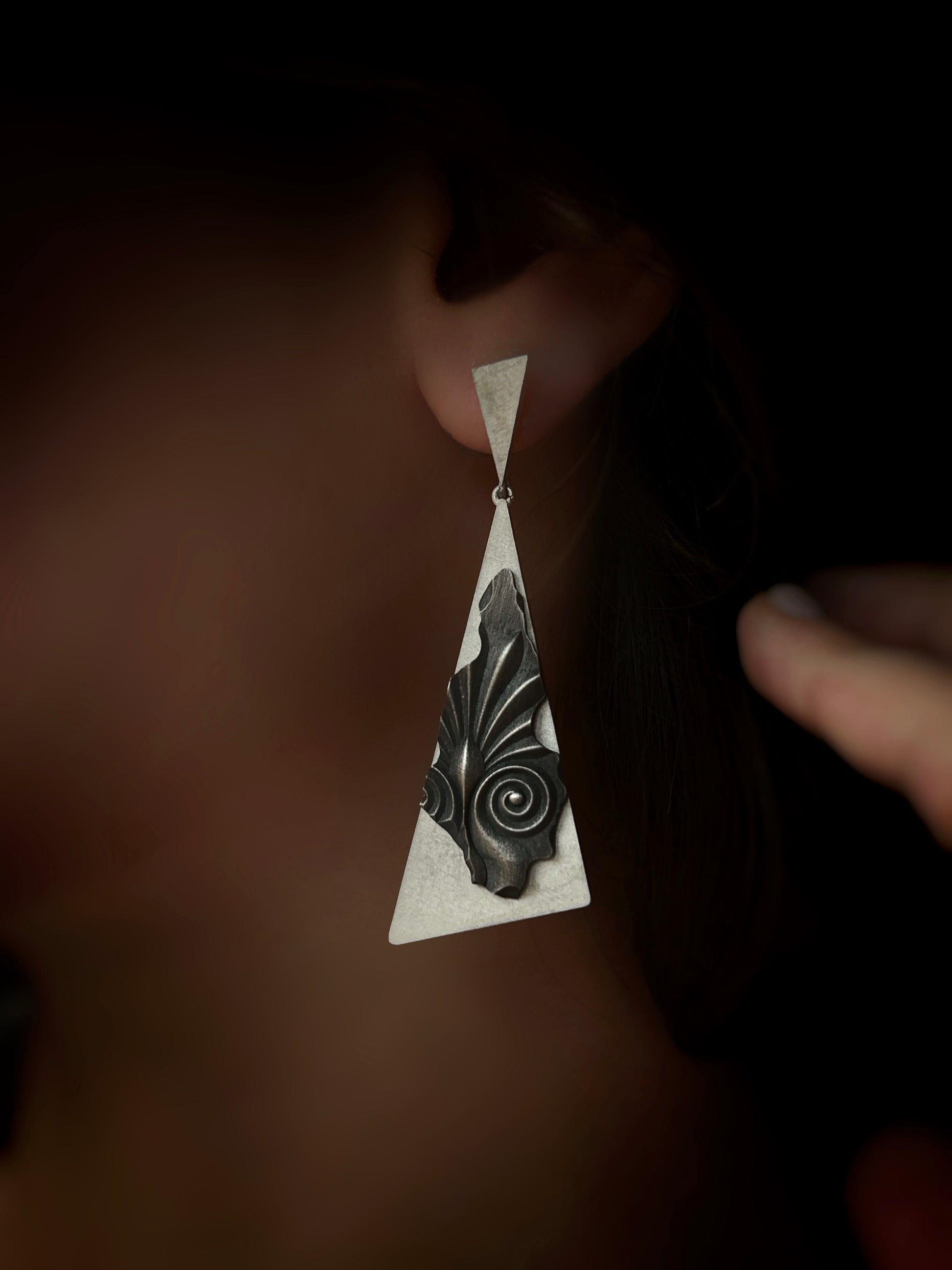 Earring with geometric design worn on an ear against a dark background