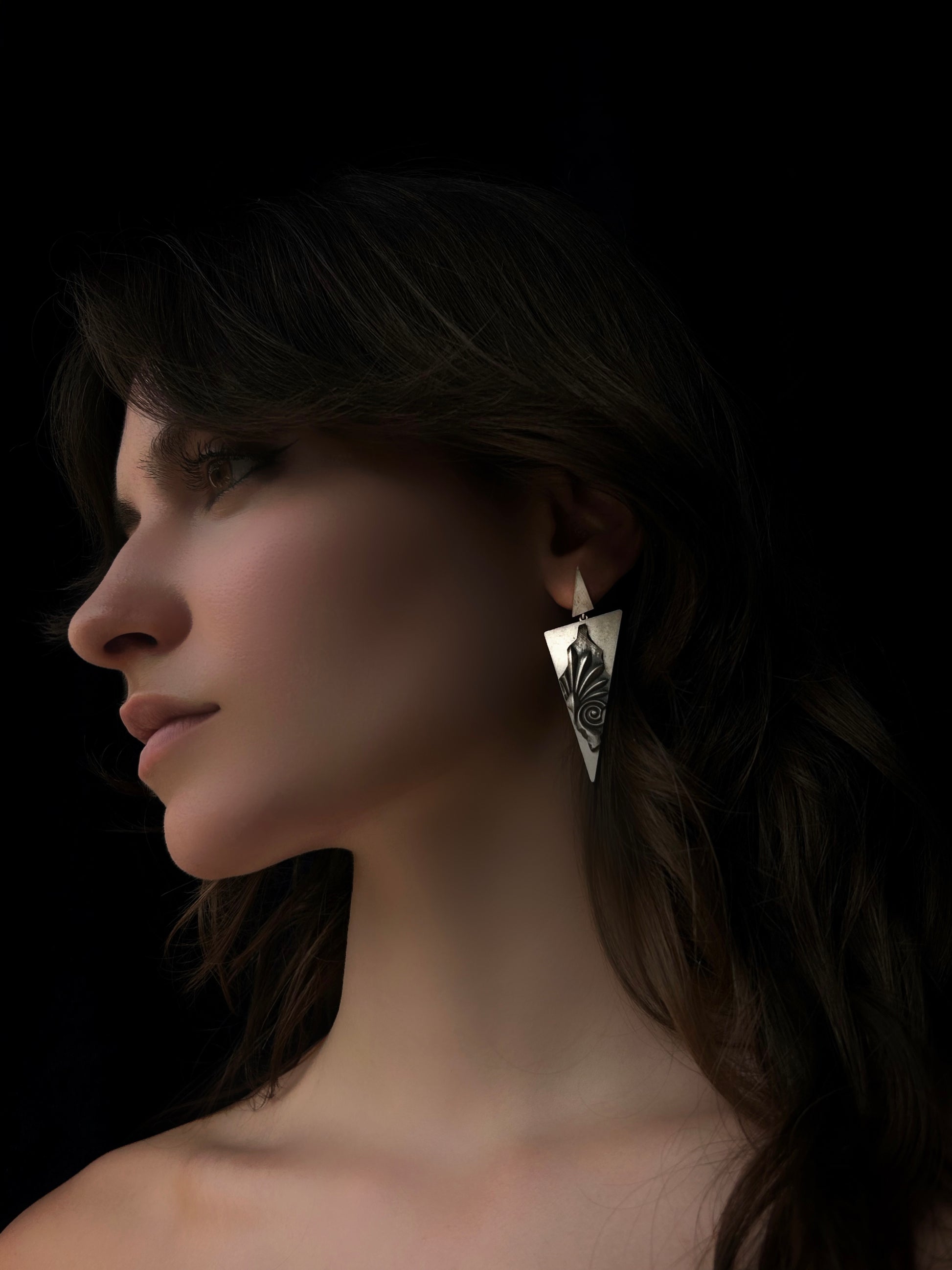Close-up of a woman wearing a unique triangular earring against a dark background