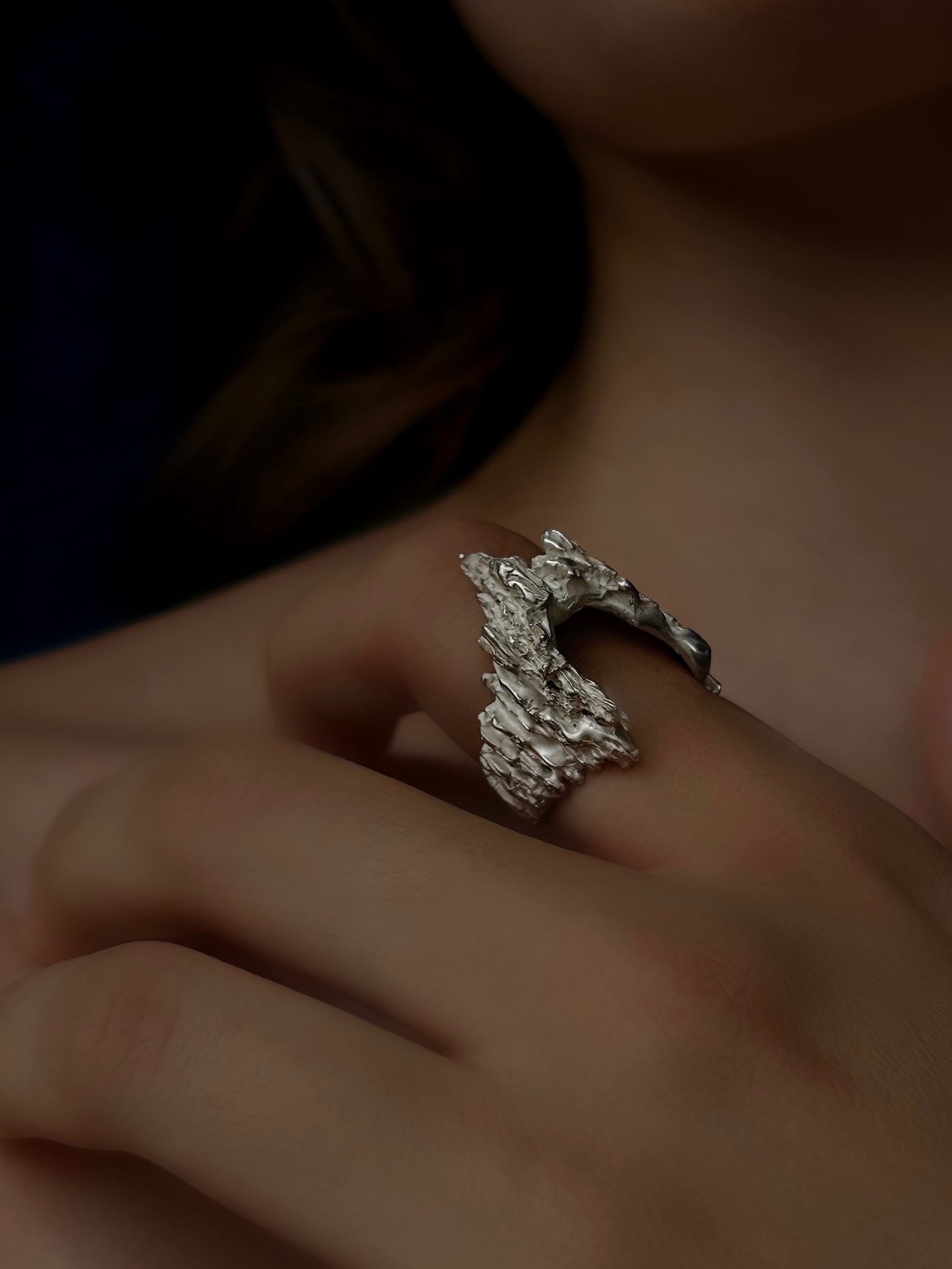 Close-up of a hand wearing a textured silver ring with a blurred background