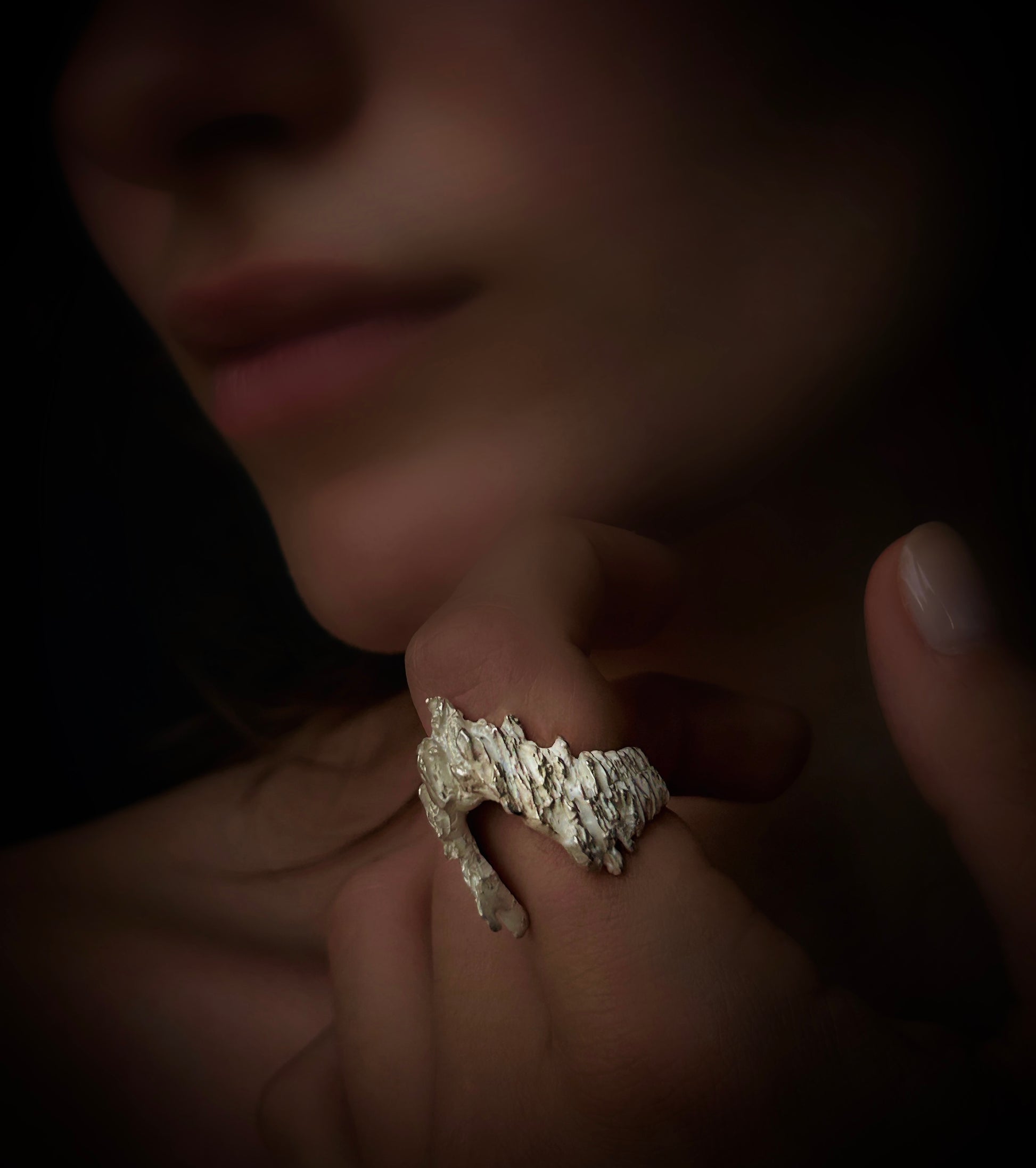 Close-up of a hand wearing a textured ring with a dark background
