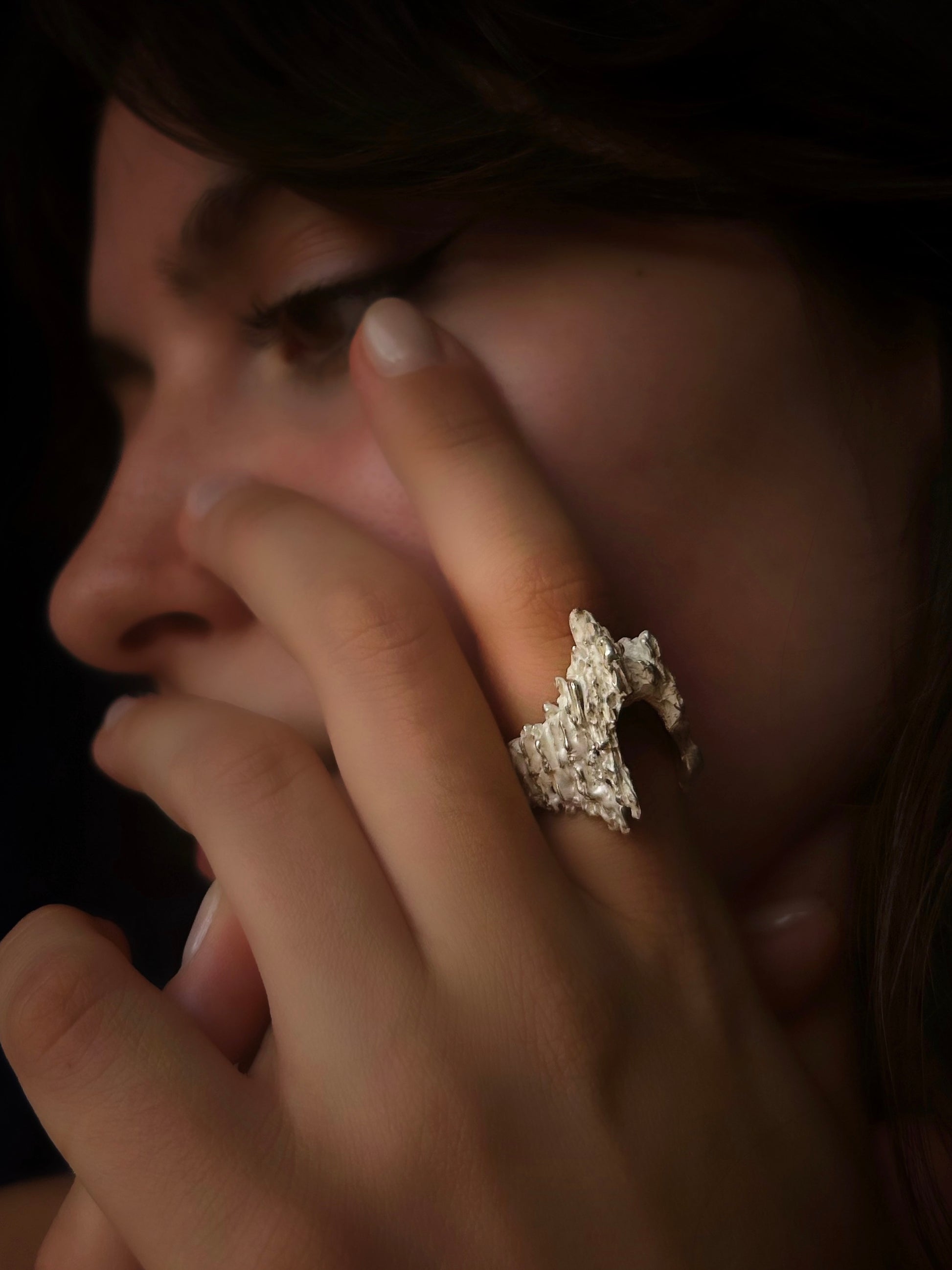 Close-up of a hand with a textured ring on a dark background