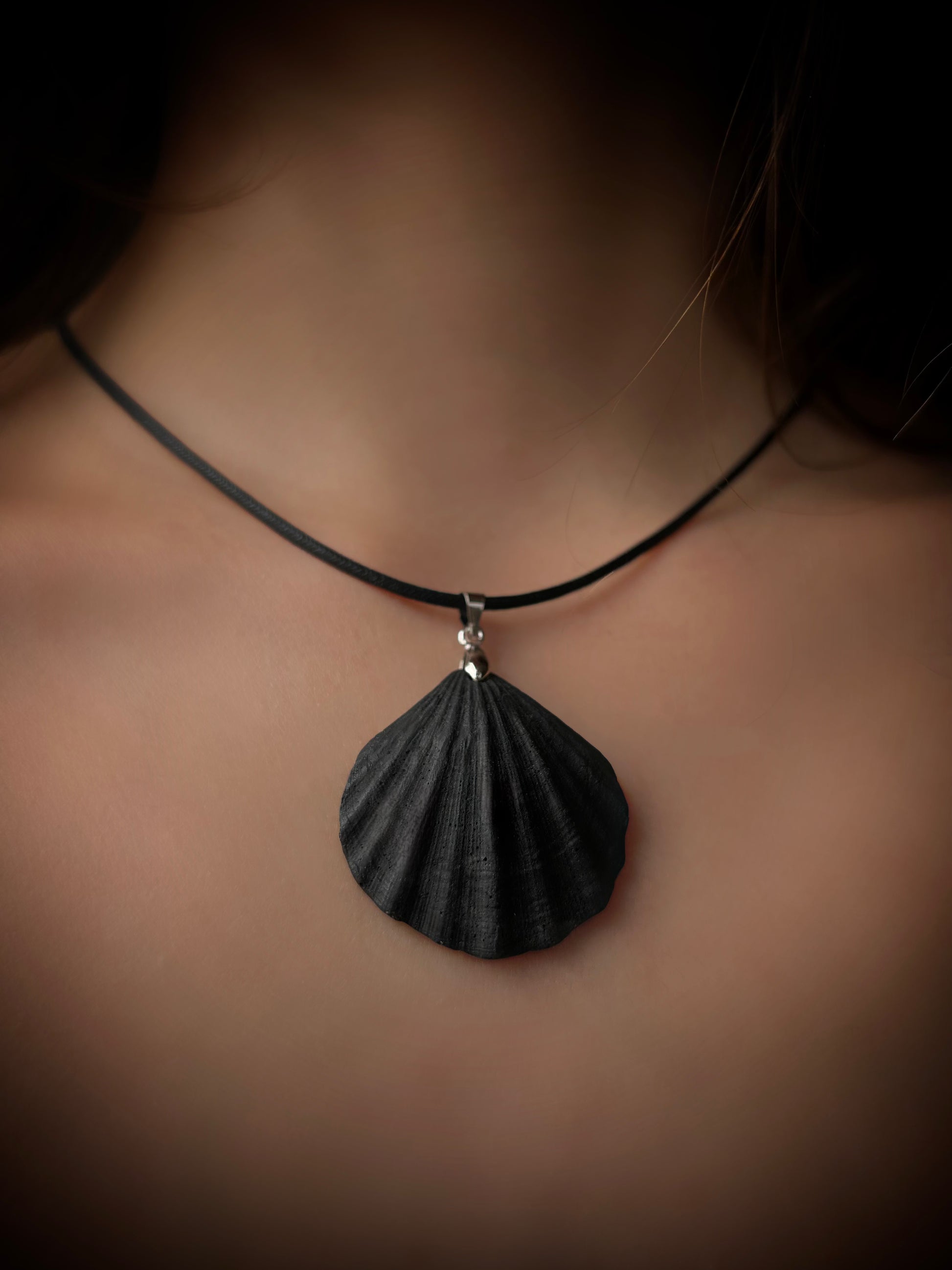 Black shell pendant necklace on a person's neck with a dark background