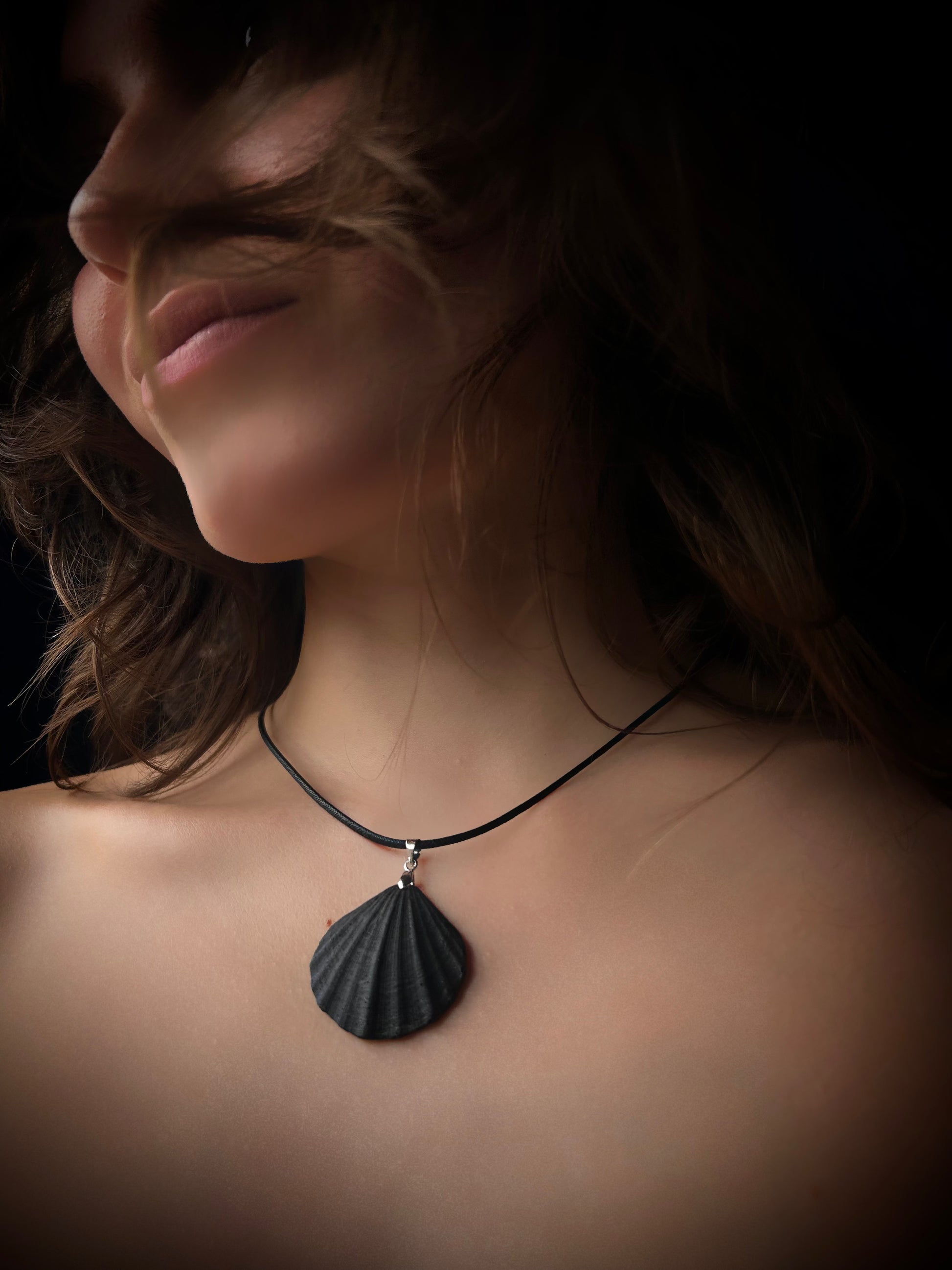Person wearing a necklace with a shell pendant against a dark background
