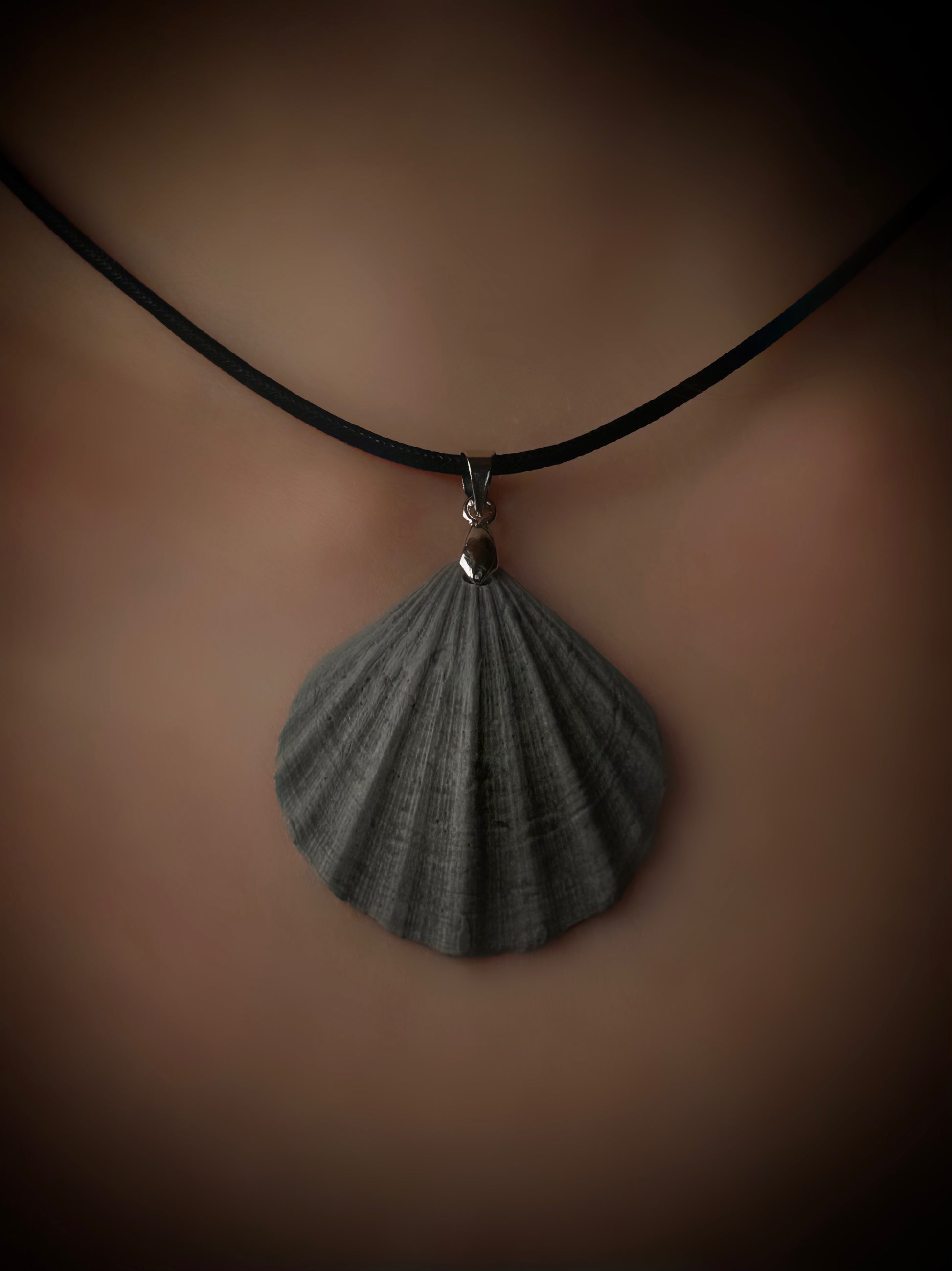 Shell pendant necklace on a black cord against a brown background