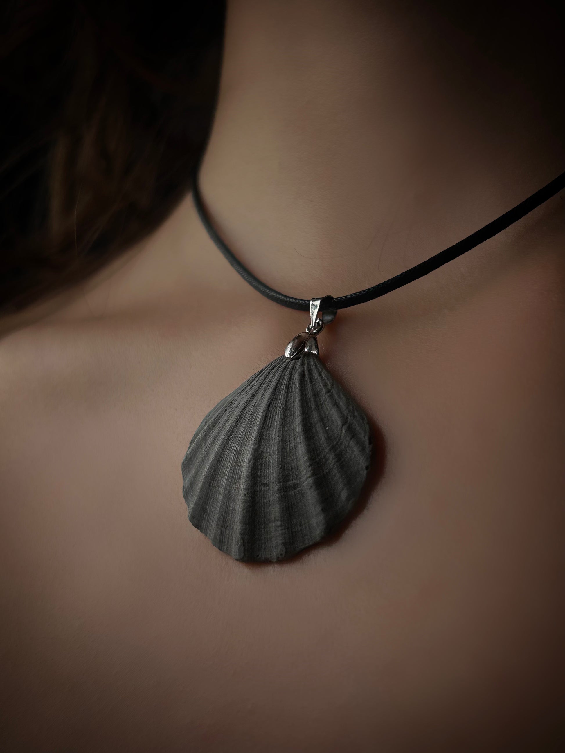 Shell pendant necklace on a person's neck against a neutral background