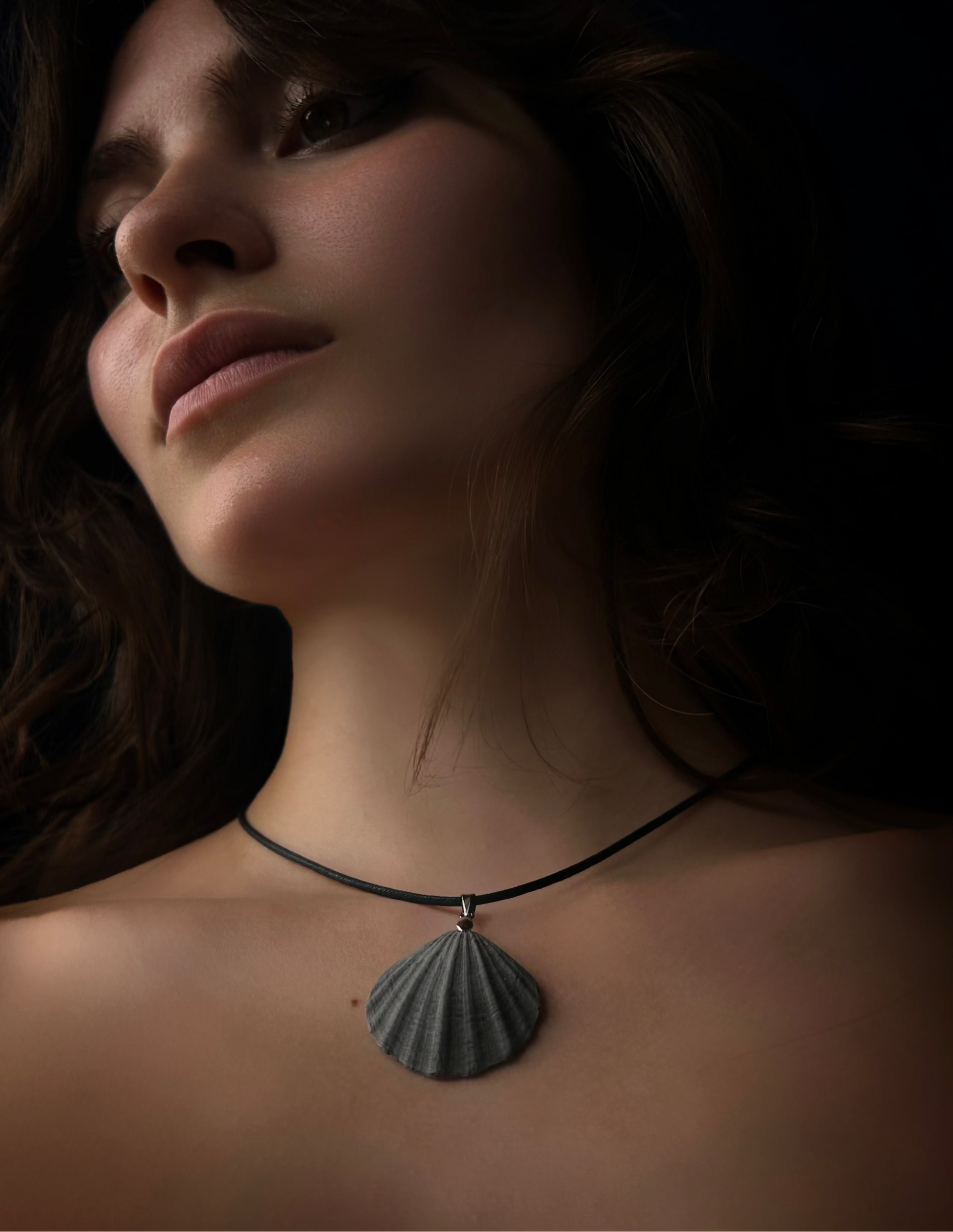 Close-up of a woman wearing a necklace with a shell pendant against a dark background