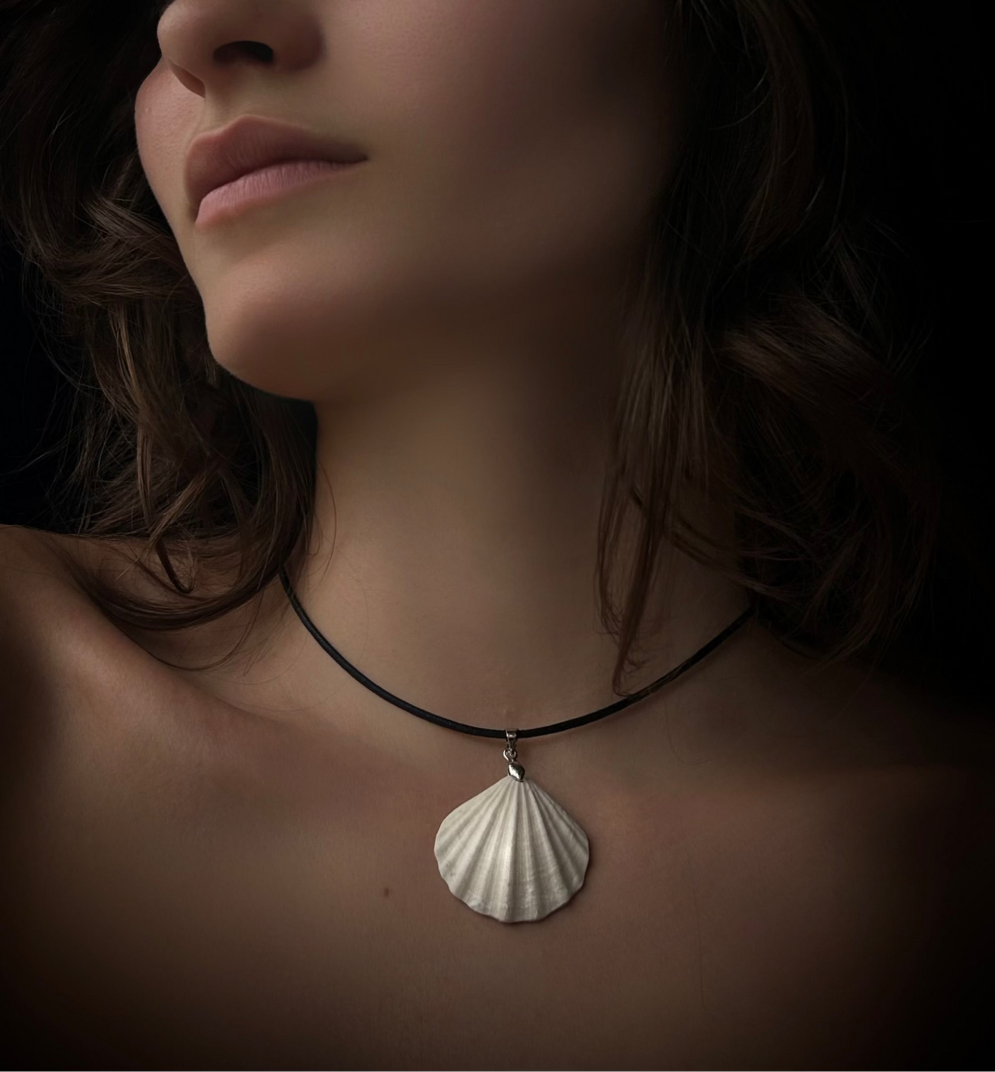 Woman wearing a necklace with a shell pendant against a dark background