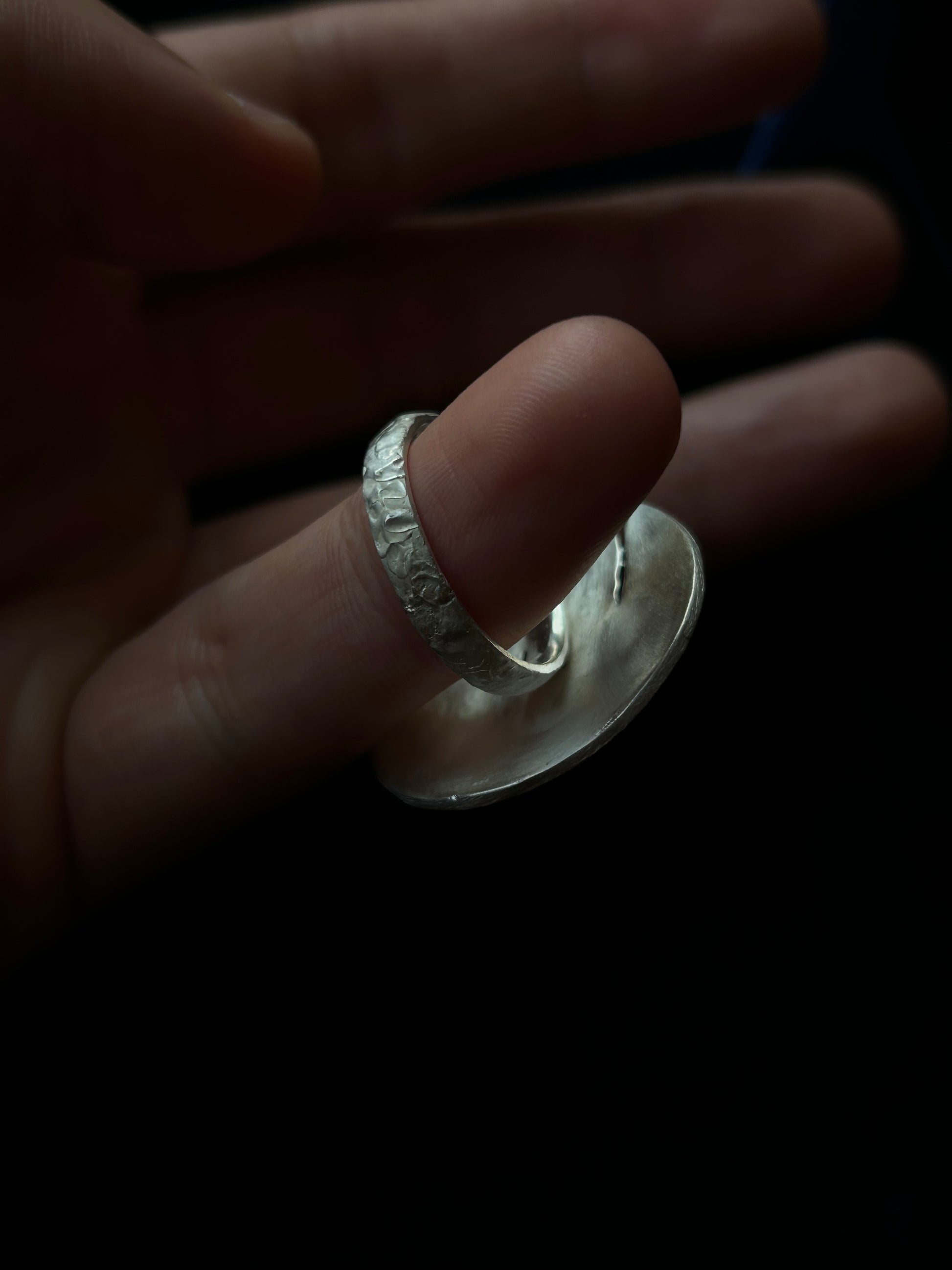 Silver ring on a finger with a dark background