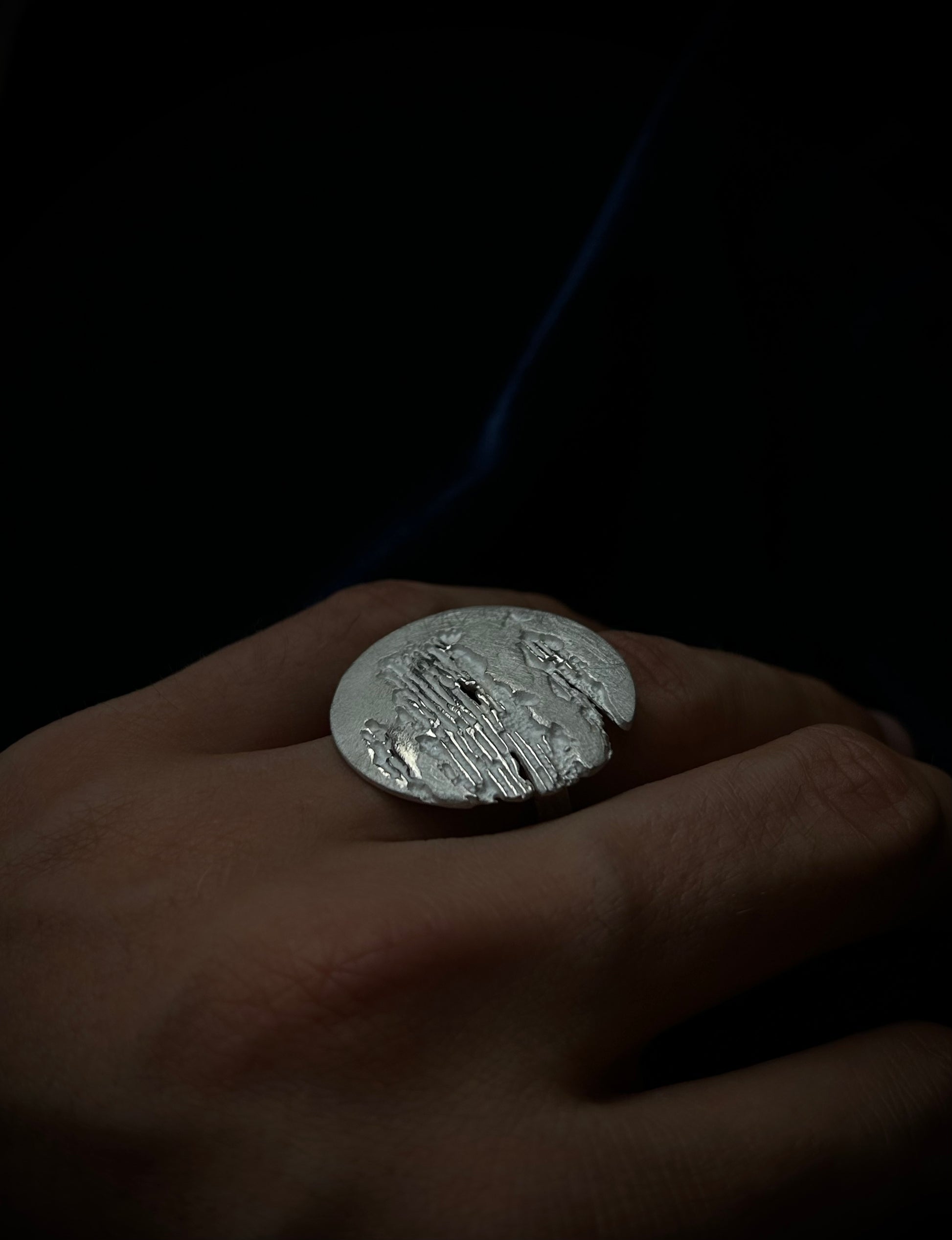 Silver ring with engraved design on a hand against a dark background