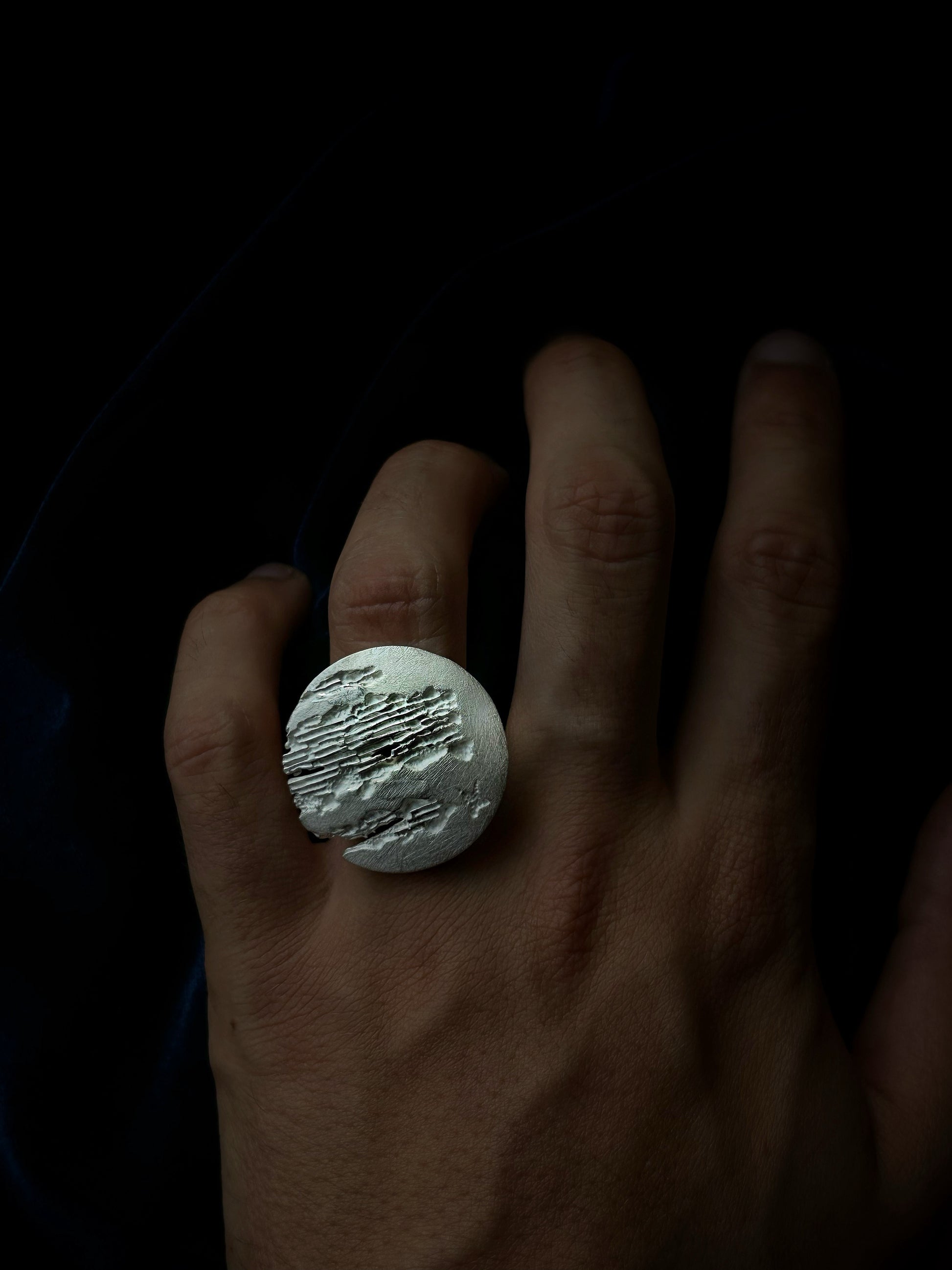 Hand wearing a silver ring with a textured design on a dark background