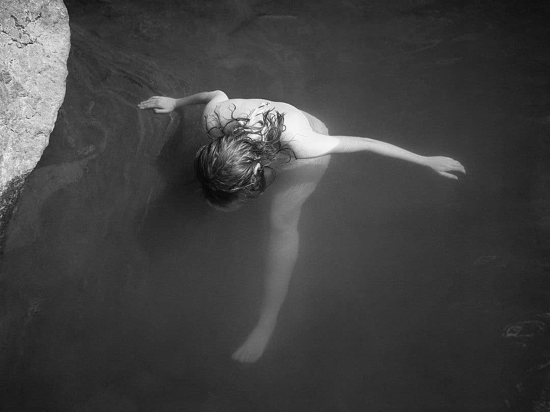 Person lying on their back in water with arms outstretched, black and white photo