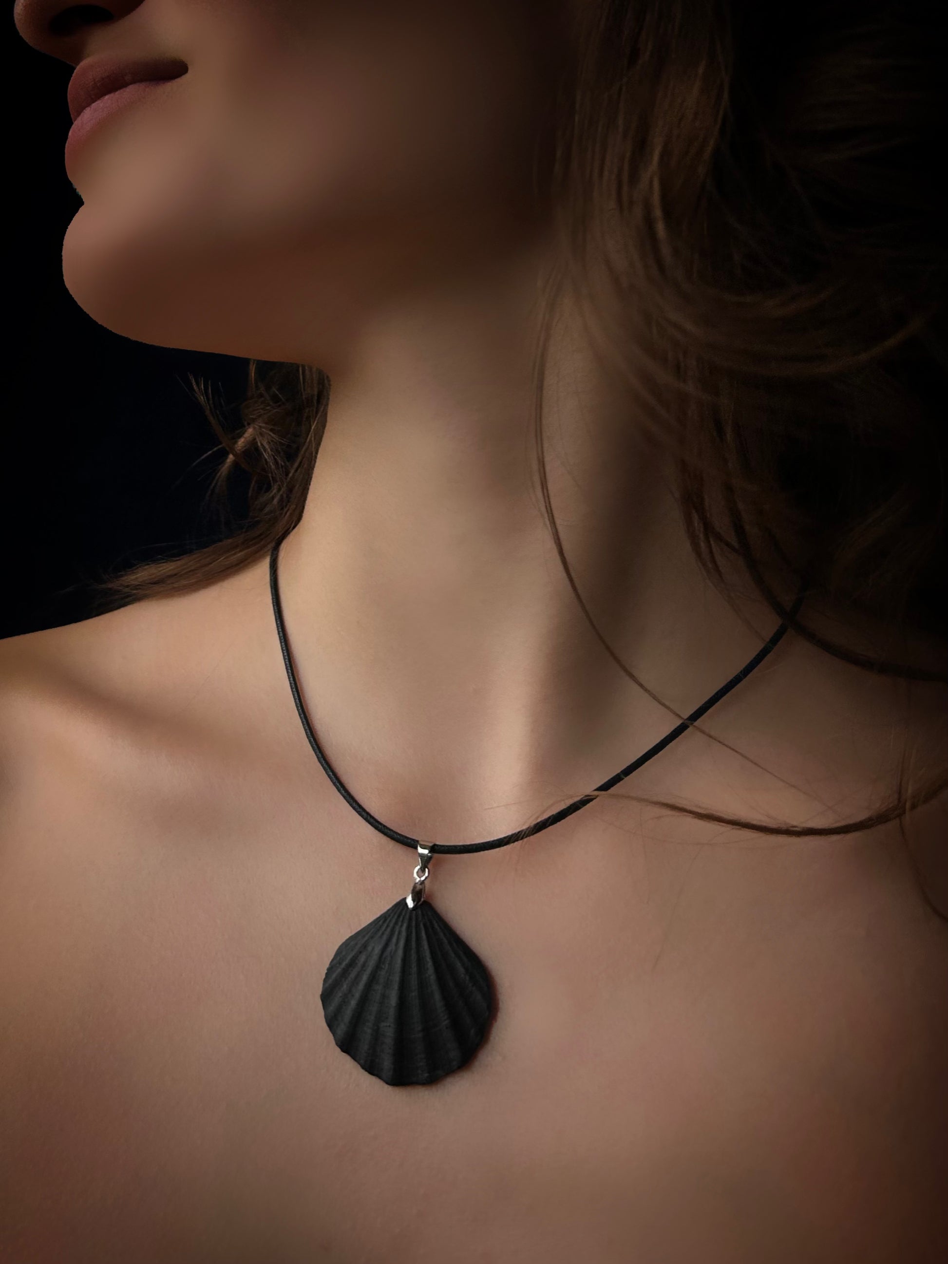 Close-up of a necklace with a black pendant on a person against a dark background