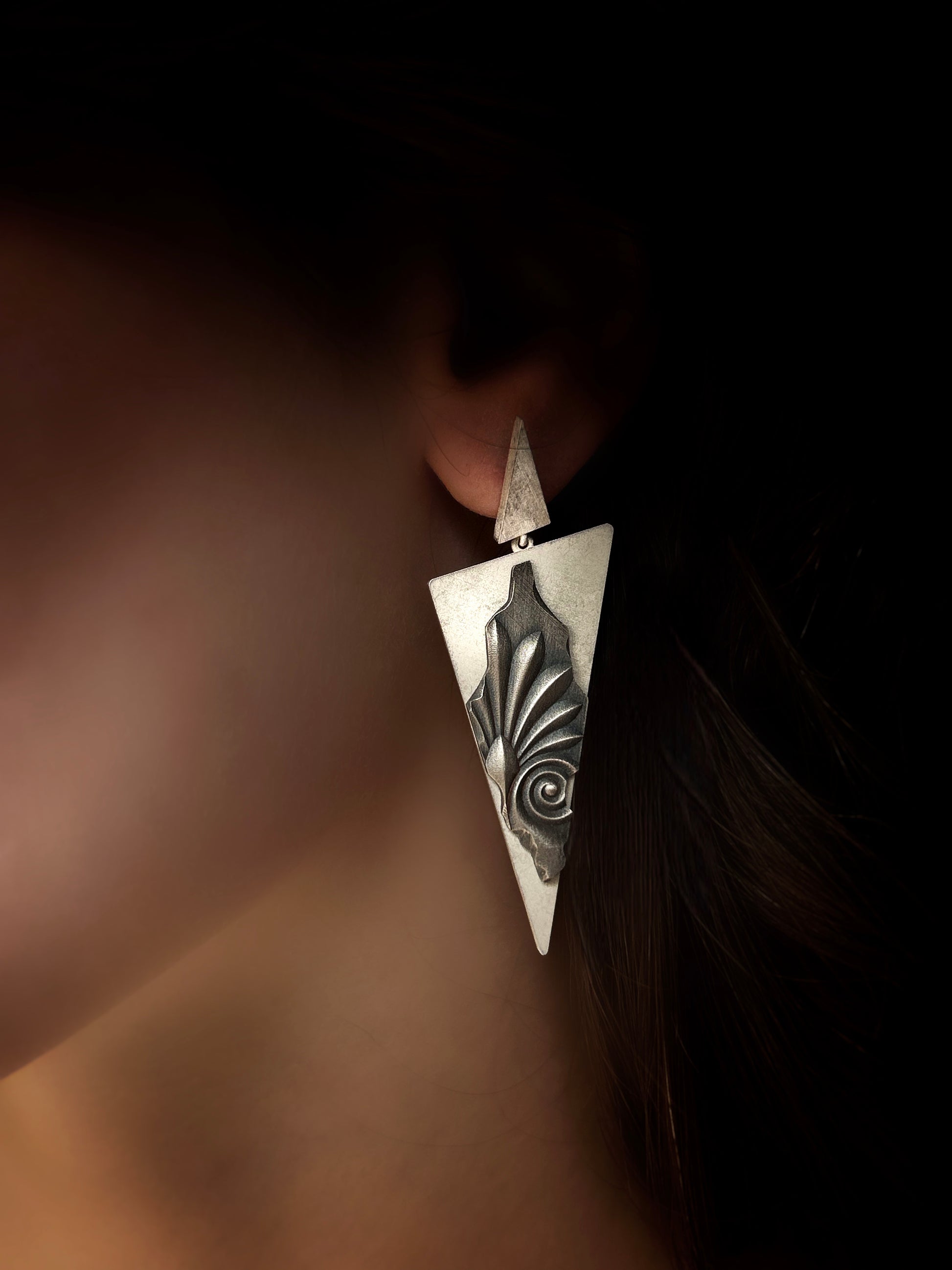 Silver earring worn on an ear with a dark background