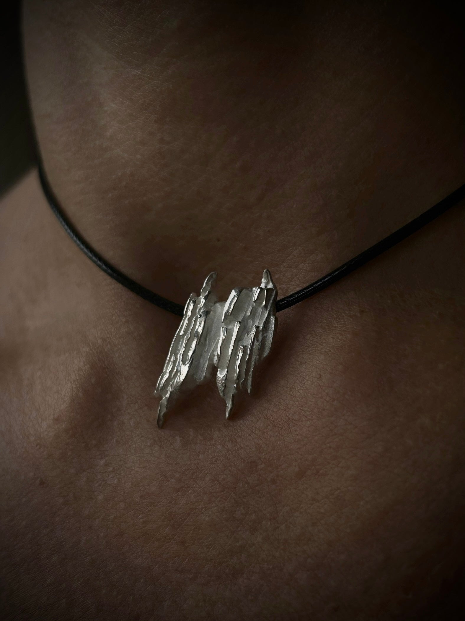 Silver pendant necklace on a black cord worn around the neck.