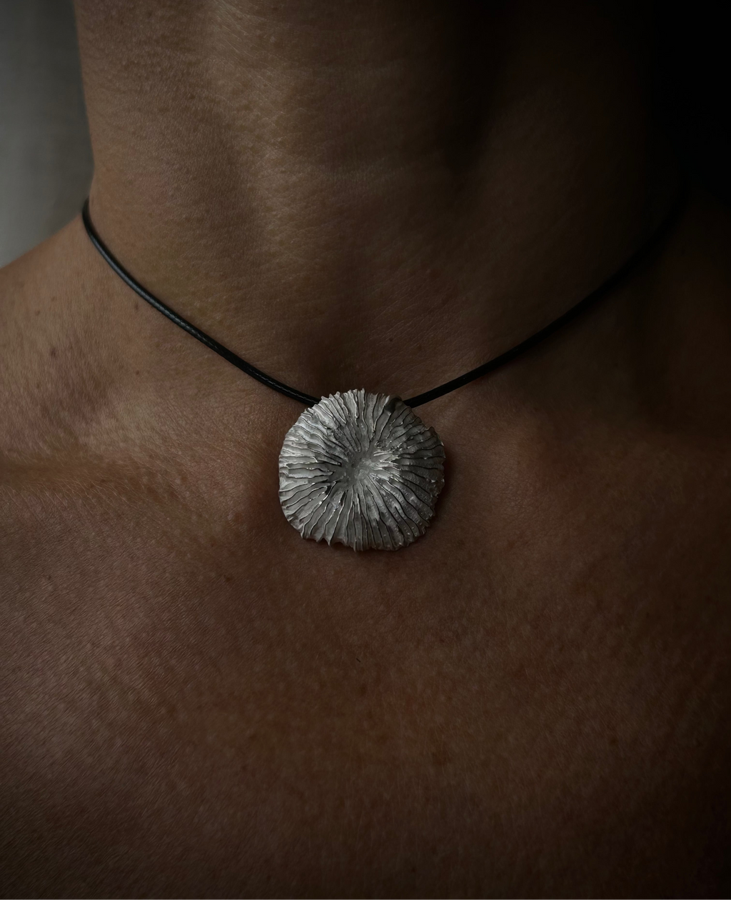 Necklace with a textured pendant on a person's neck against a dark background