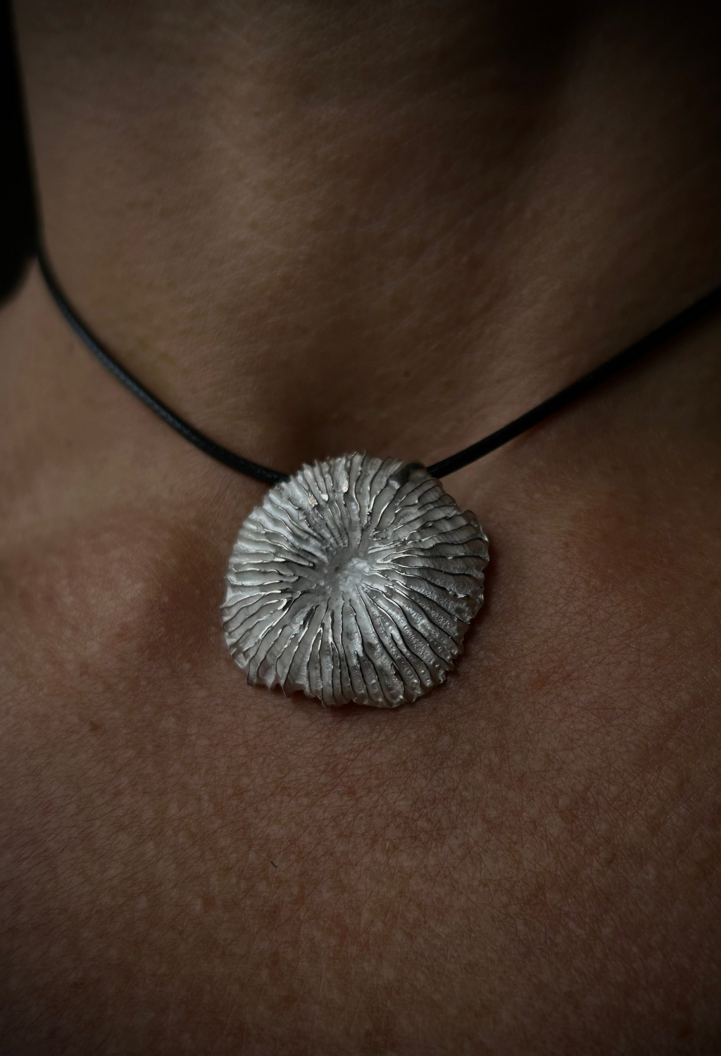 Silver pendant necklace on a person's neck with a dark background