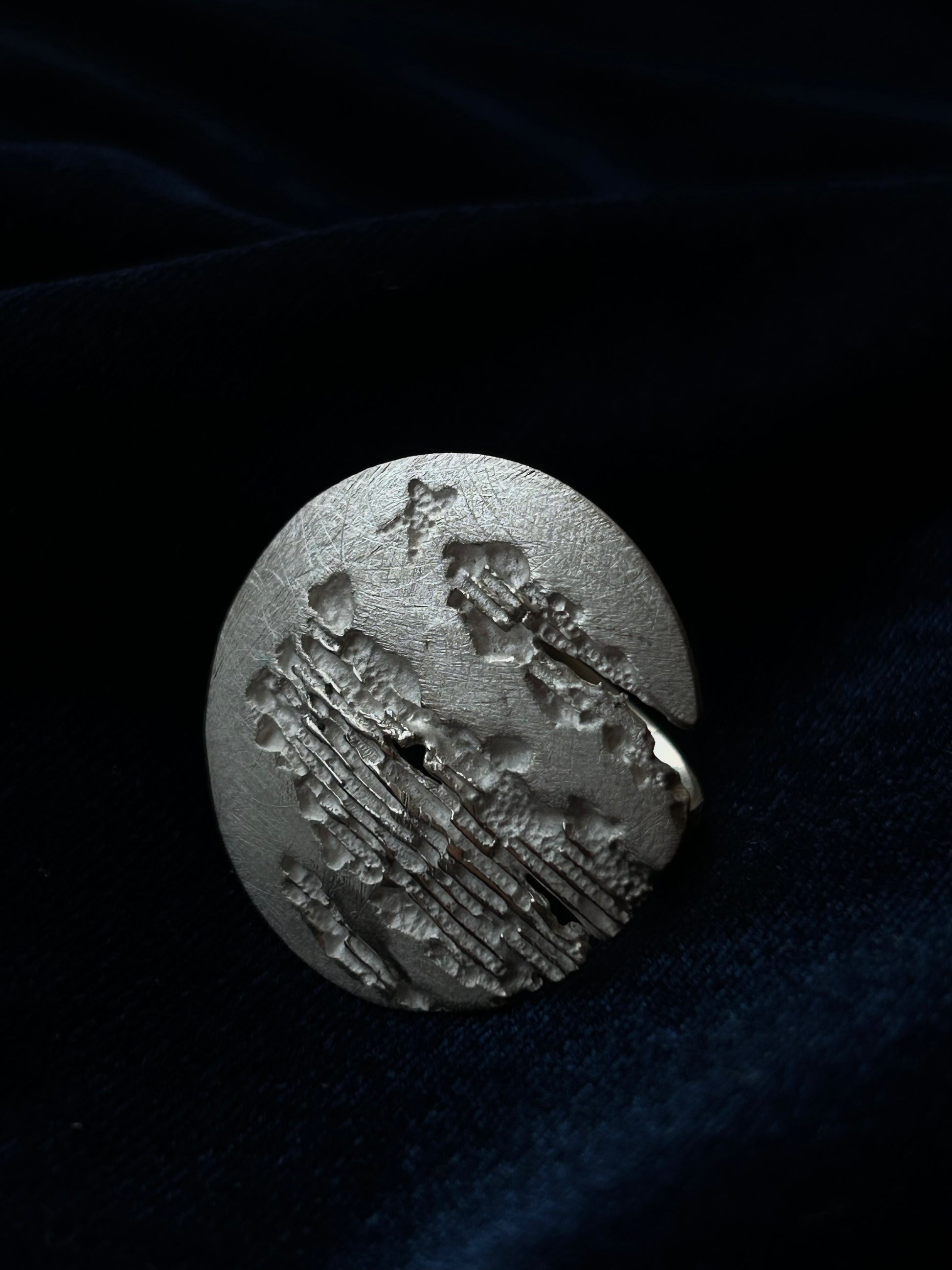 Silver ring with intricate design on a dark fabric background
