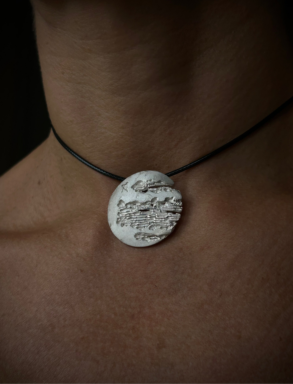 Necklace with a round pendant on a person's neck against a dark background