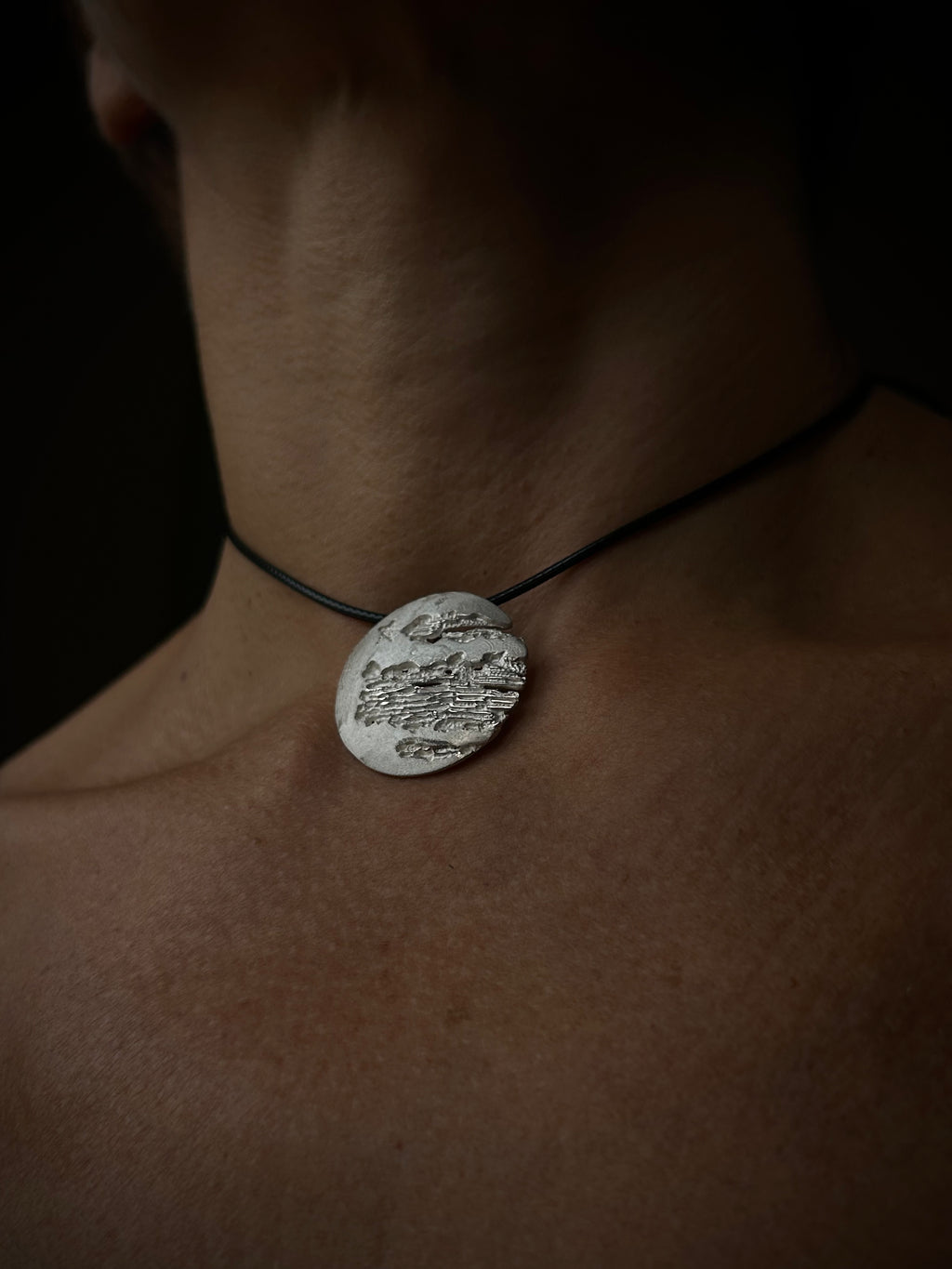 Necklace with a round pendant on a person's neck against a dark background