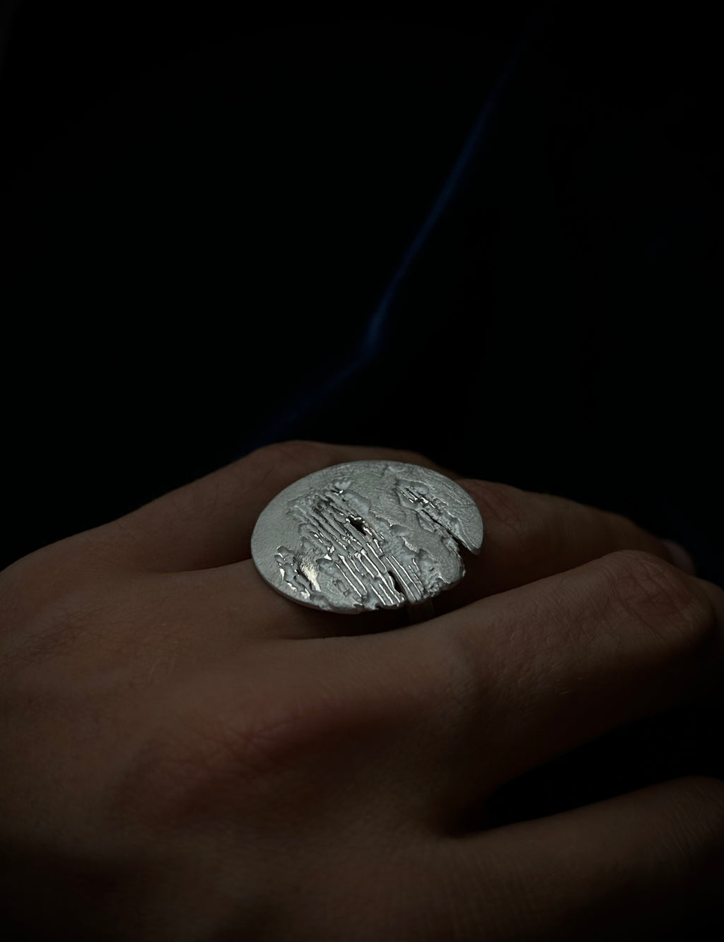 Silver ring with engraved design on a hand against a dark background