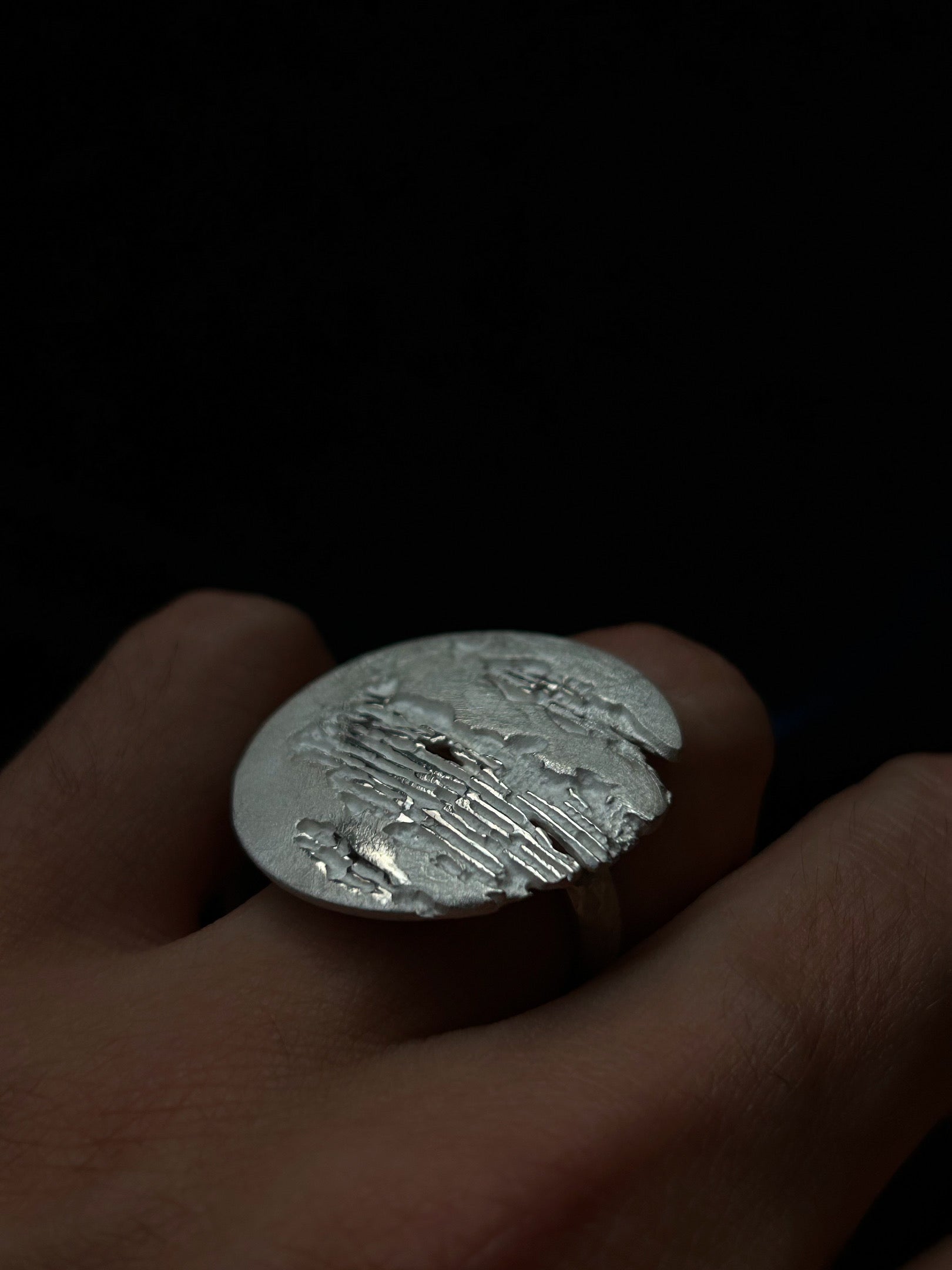 Silver jewel held in a hand against a dark background