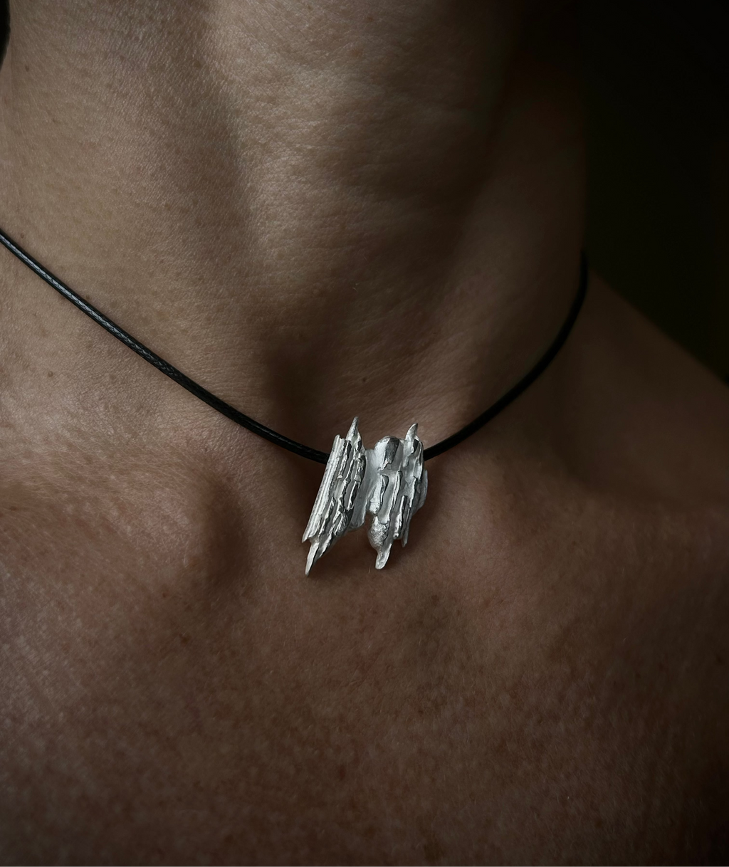 Silver pendant on a black cord necklace worn by a person with a dark background