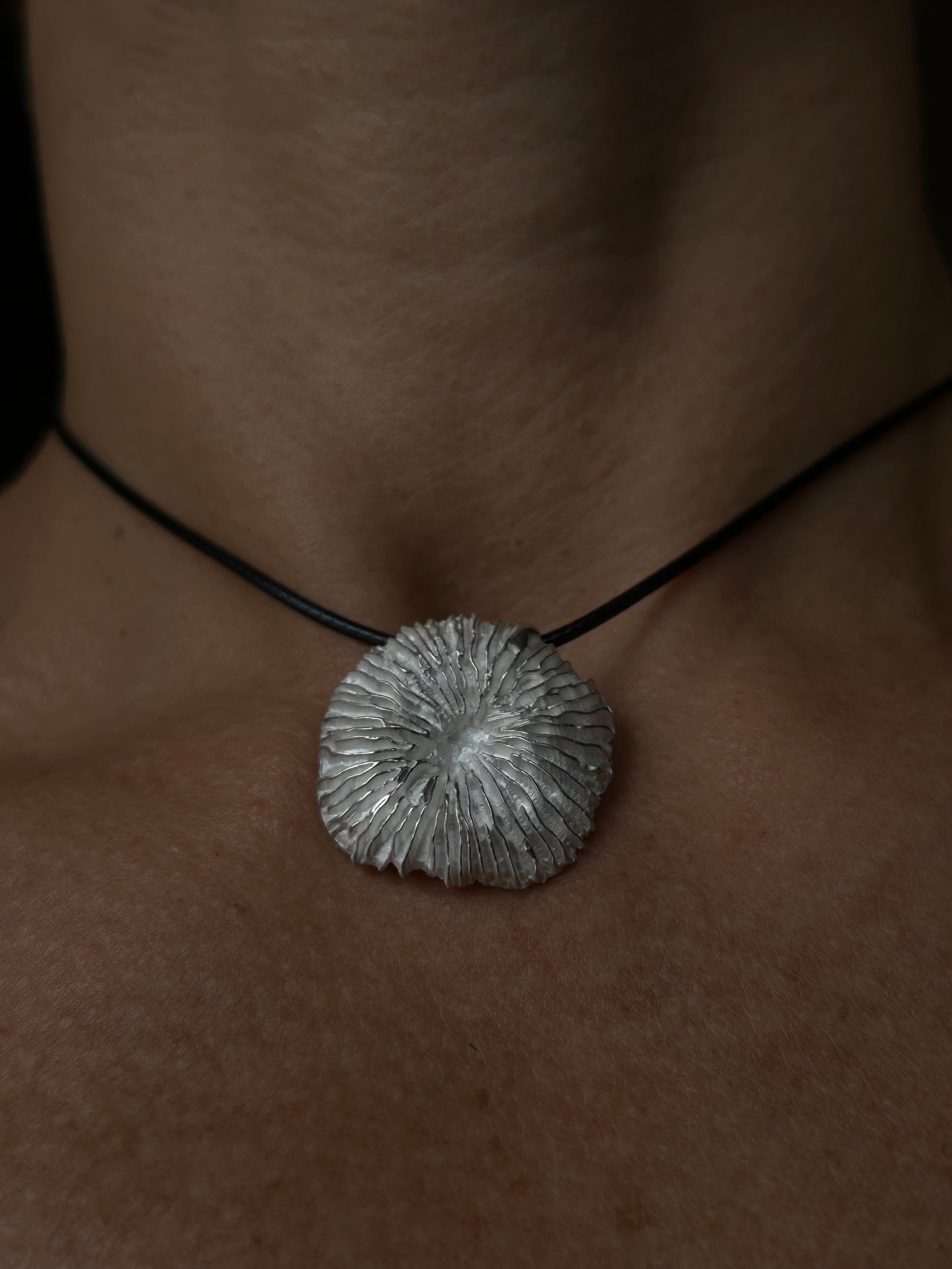 Necklace with a textured silver pendant on a person's neck against a dark background