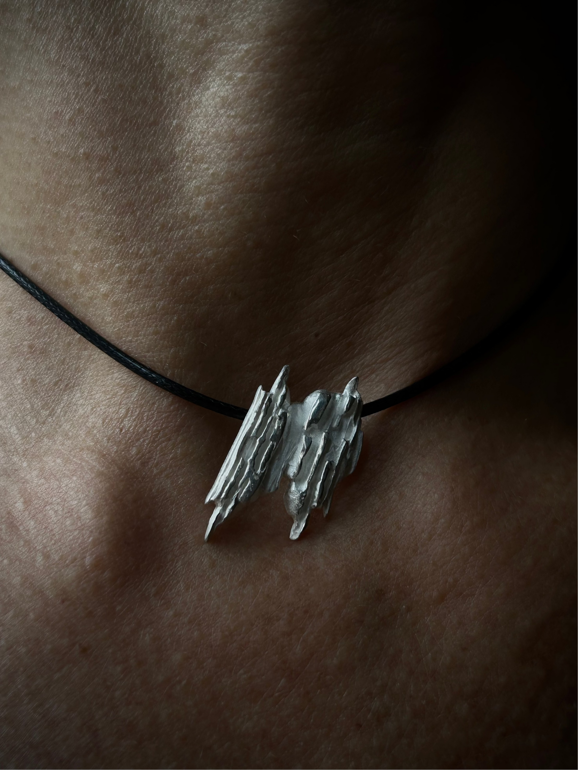 Silver pendant on a black cord against a skin background